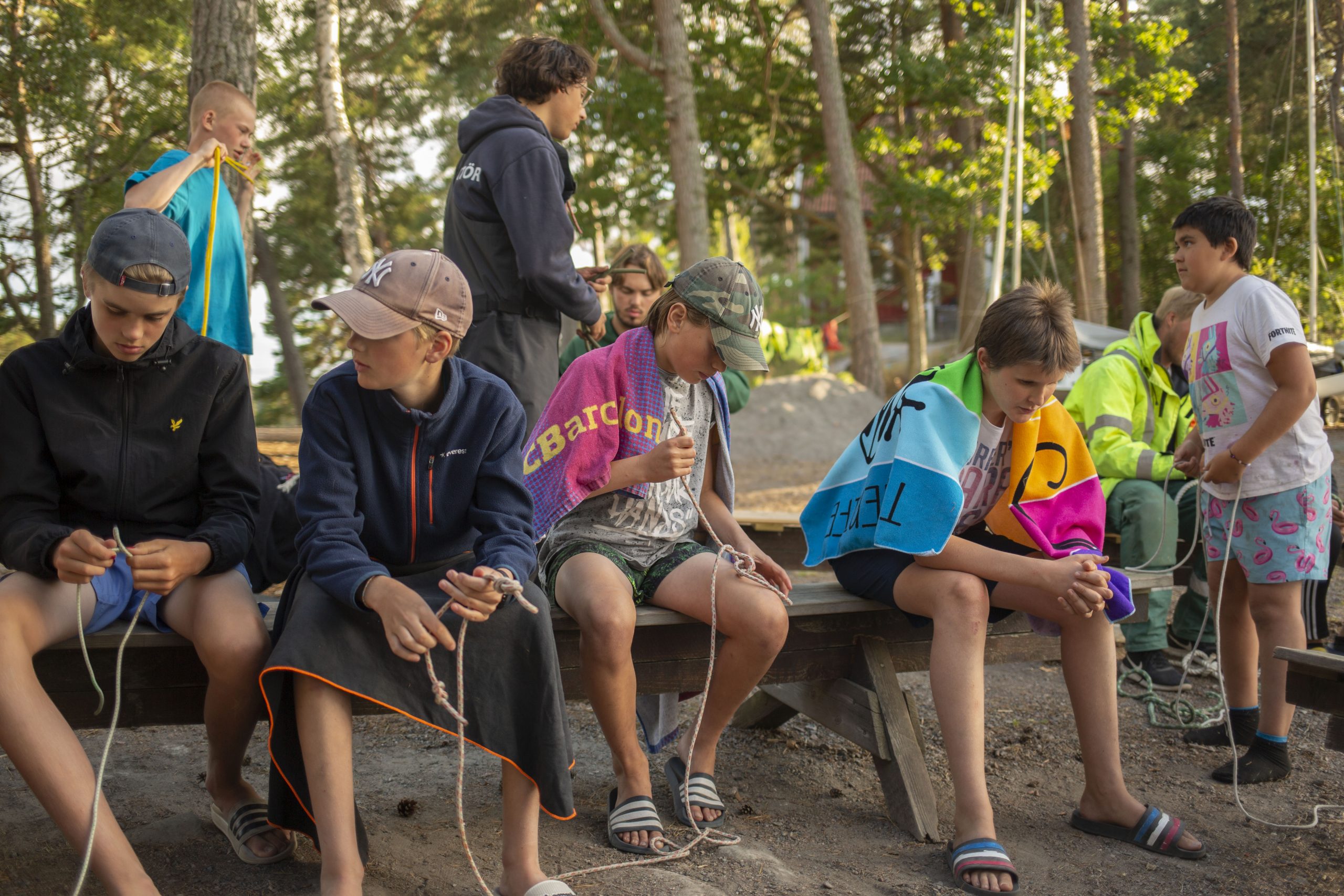 En grupp deltagare på KFUM Ängsholmens sommarläger som sitter och lär sig knopar inför stundande på ett av KFUM Ängsholmens sommarläger.